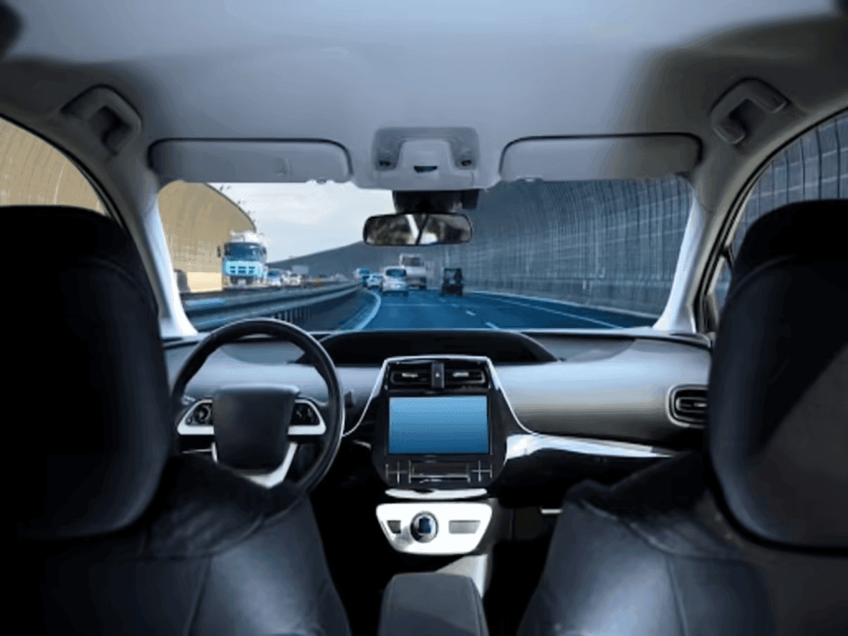 Interior view from the back seat of a car showing the dashboard, steering wheel, and windshield with a highway and tunnel visible ahead